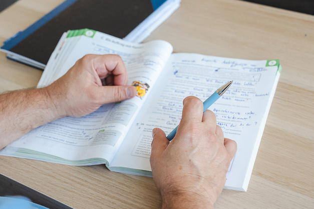 Hände mit Stift über einem offenen Buch.