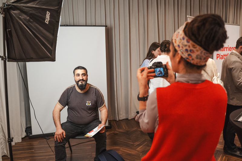Ein Mann sitzt auf einem Stuhl und wird von einer Person mit einer Kamera fotografiert.