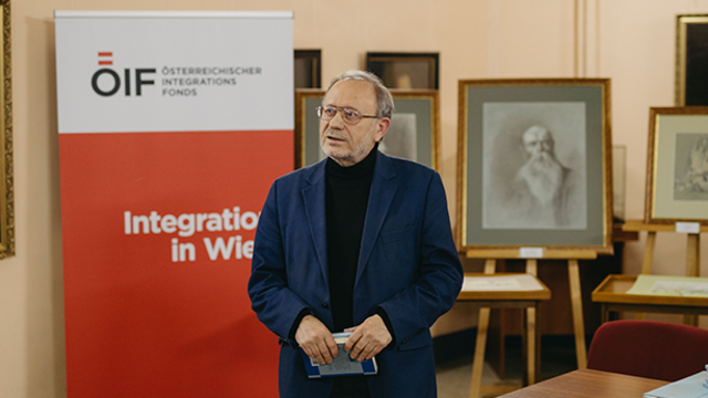 Ein Mann steht vor einem roten Banner des Österreichischen Integrationsfonds und spricht über Integration in Wien.