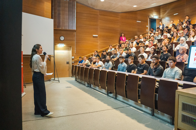Eine Referentin spricht vor einer großen Gruppe von Zuhörern in einem Veranstaltungssaal.