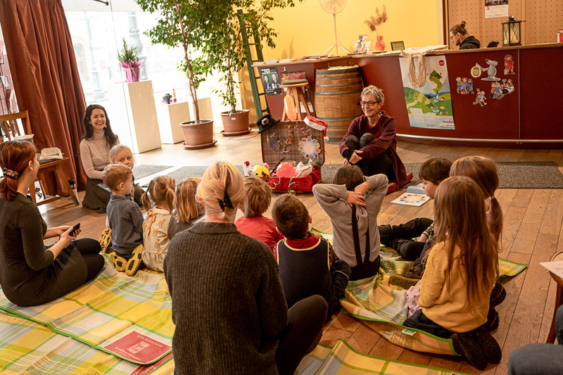 Eine Erzählerin sitzt vor einer Gruppe von Kindern in einem gemütlichen Raum.