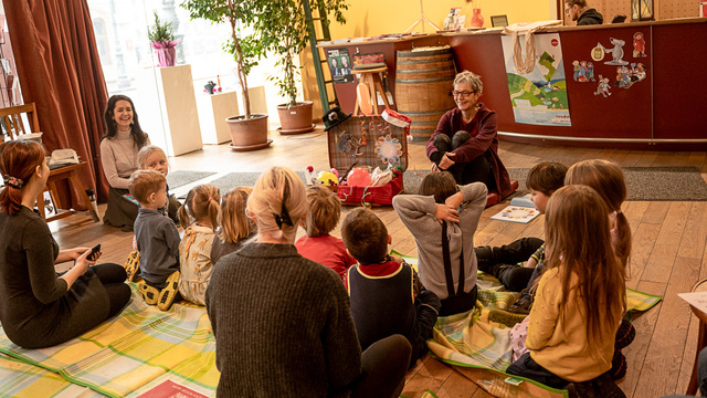Eine Erzählerin sitzt vor einer Gruppe von Kindern in einem gemütlichen Raum.