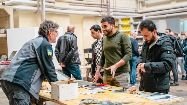 Gruppe von Menschen diskutiert an einem Tisch mit verschiedenen Materialien in einer Werkstatt.