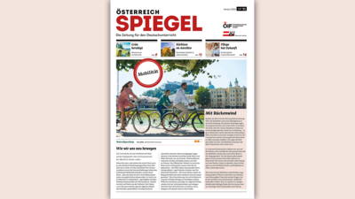 Zwei Personen fahren mit Fahrrädern an einer schönen Uferpromenade vorbei, mit einer Stadtansicht im Hintergrund.