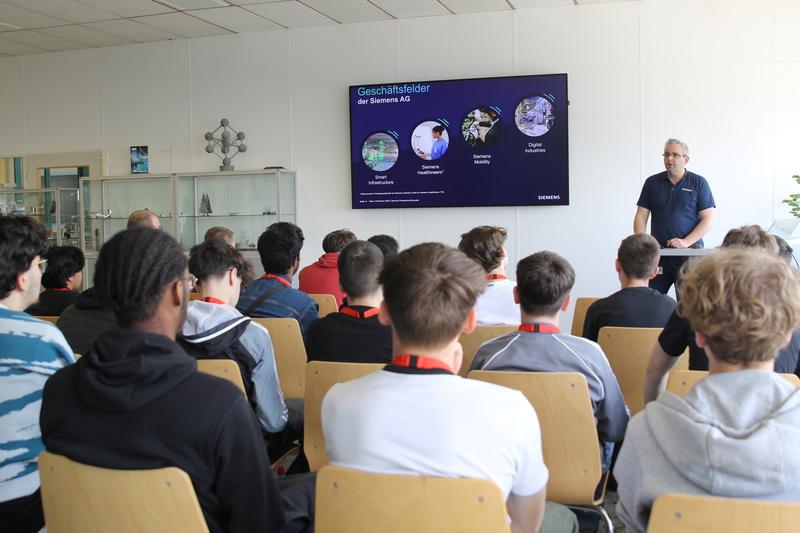 Eine Präsentation über die Geschäftsbereiche der Siemens AG vor einer Gruppe von Zuhörern.
