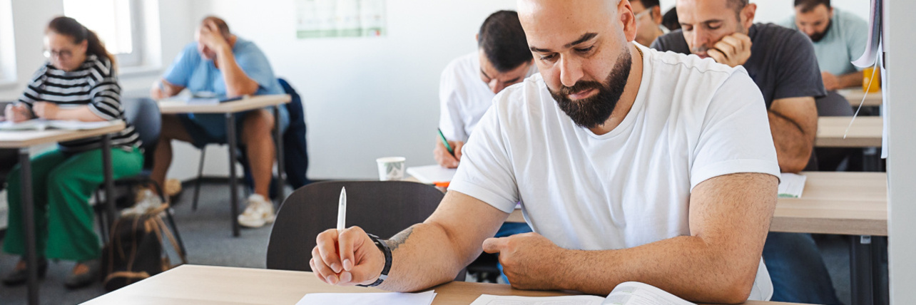 Mann schreibt in einem Unterrichtsraum.