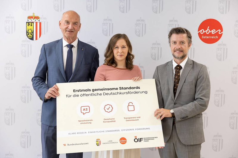 Integrationslandesrat Dr. Christian Dörfel, Bundesministerin Claudia Bauer und ÖIF-Direktor Franz Wolf präsentieren gemeinsam eine Informationstafel zu einheitlichen Standards für die öffentliche Deutschkursförderung.