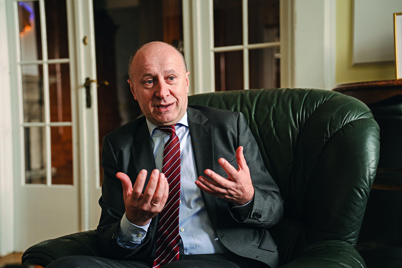 Ein Mann in Anzug sitzt auf einem Sessel und gestikuliert während eines Gesprächs.