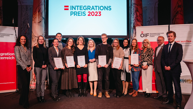 Gruppenfoto von Preisträgern des Integrationspreises 2023 mit Zertifikaten, vor einer Bildschirmpräsentation.