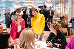 Zwei Frauen im Gespräch, eine in gelber Jacke, andere in pinkem Anzug, umgeben von interessierten Zuhörern.