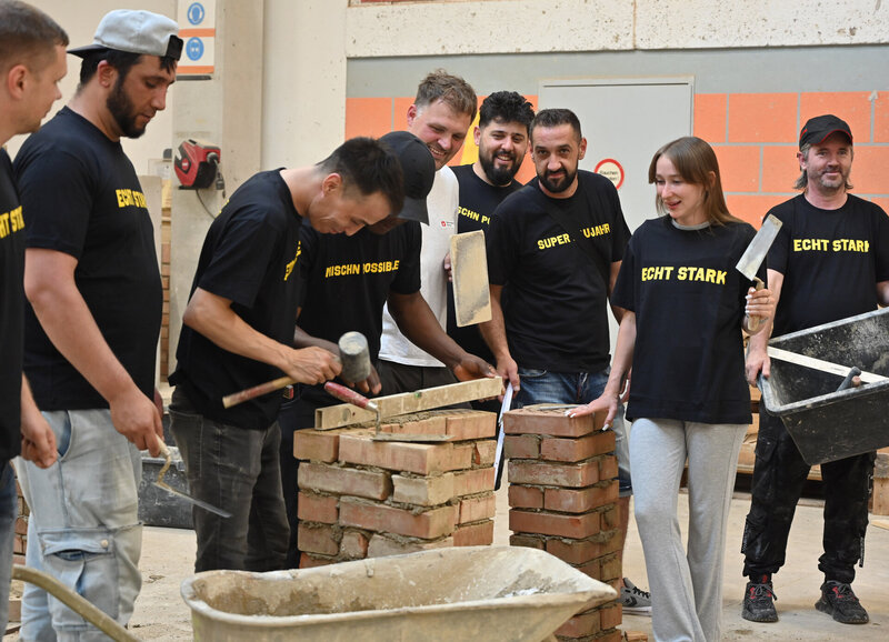 Gruppe von Arbeitern in schwarzen Shirts beim Ziegelmauern während Schulung