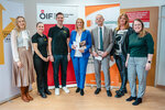 Eine Gruppe von sechs Personen steht zusammen und hält Informationsmaterialien in einer Büroumgebung.