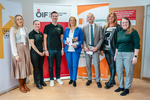 Eine Gruppe von sechs Personen steht zusammen und hält Informationsmaterialien in einer Büroumgebung.