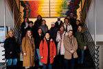 Eine Gruppe von 19 Frauen posiert lächelnd auf einer Treppe vor einem bunten Wandbild.