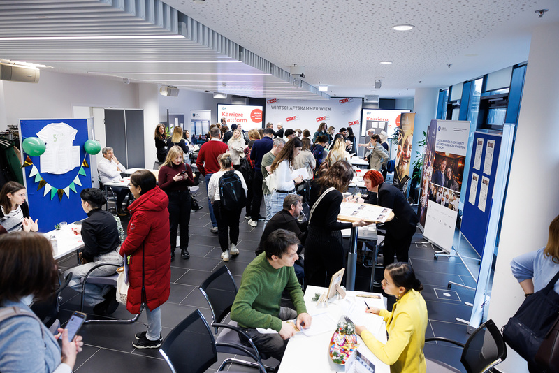 Ein überfüllter Raum mit Menschen, die Informationen an Ständen für Karriere- und Ausbildungsmöglichkeiten suchen.