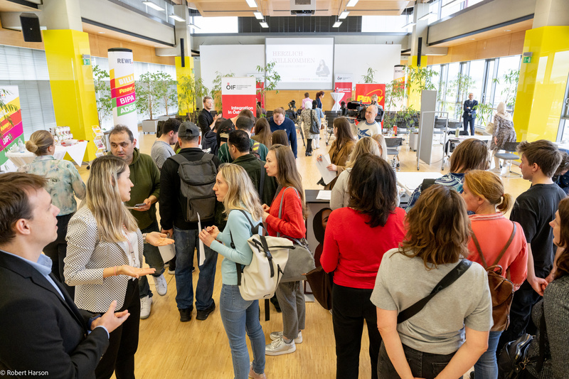 Eine Gruppe von Menschen unterhält sich in einem hellen Raum mit Informationsständen.