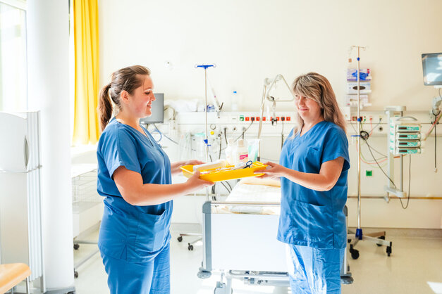 Zwei Krankenschwestern tauschen ein Tablett in einem Raum.