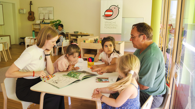 Eine Lehrerin erklärt Kindern ein Buch am Tisch in einem kreativen Lernraum.
