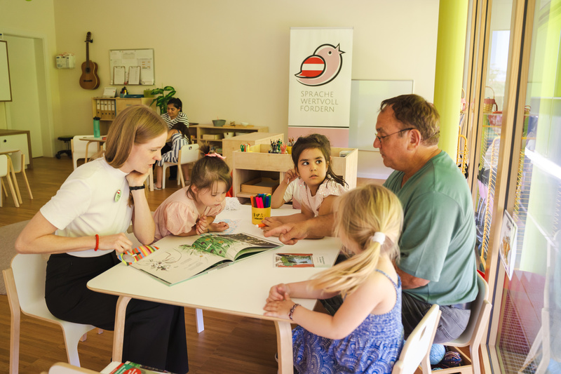 Eine Lehrerin erklärt Kindern ein Buch am Tisch in einem kreativen Lernraum.
