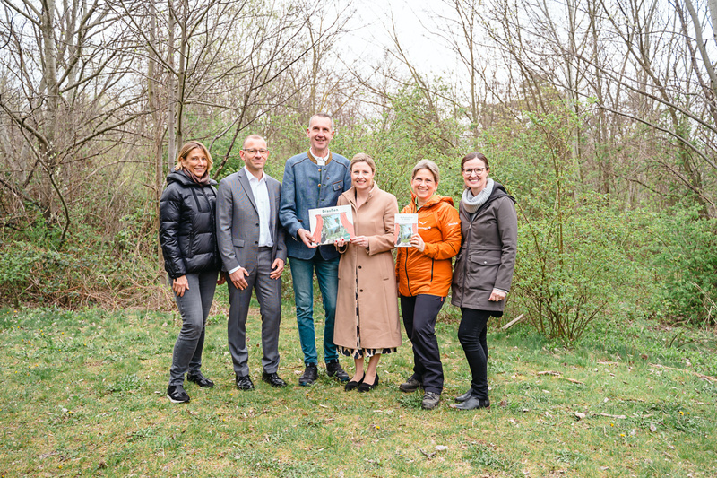 Sechs Personen stehen in einem Wald und halten Bücher in den Händen.
