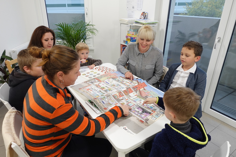 Eine Gruppe von Erwachsenen und Kindern diskutiert über einen großen Plan auf einem Tisch.