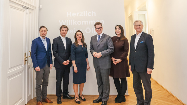 Sechs Personen posieren vor einer Wand mit dem Schriftzug "Herzlich Willkommen bei Öl".