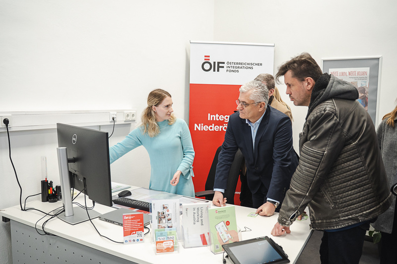 Eine Person erklärt etwas am Computer einer Gruppe von Menschen in einem Büro für Integration.