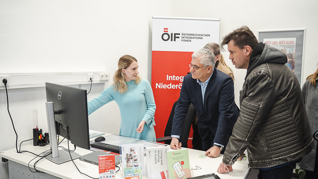 Eine Person erklärt etwas am Computer einer Gruppe von Menschen in einem Büro für Integration.