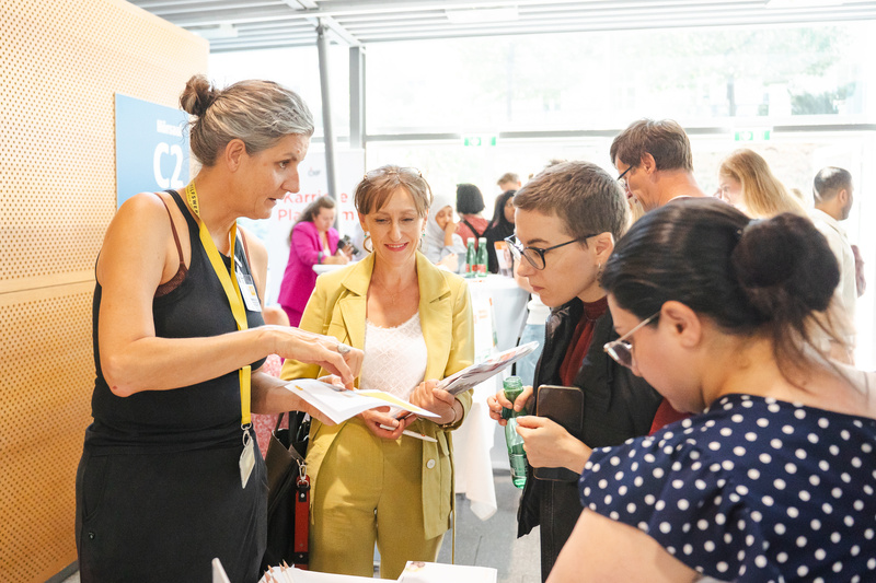 Eine Gruppe von Menschen diskutiert und schaut sich Unterlagen bei einer Veranstaltung an.