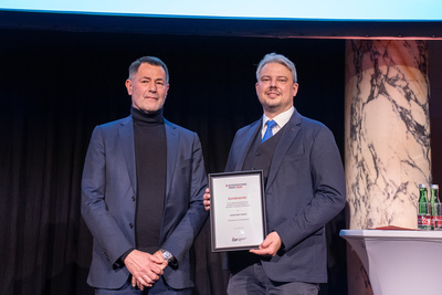 Zwei Männer stehen auf einer Bühne und halten einen Preis für den Sonderpreis 2024 in den Händen.