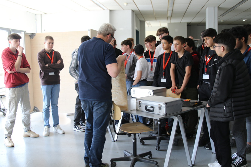 Eine Gruppe von Jugendlichen beobachtet aufmerksam einen Vortragenden, der ein Material zeigt.