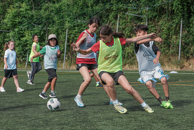 Eine Gruppe von Kindern spielt Fußball auf einem Kunstrasenplatz. Einige dribbeln, während andere versuchen, den Ball zu erobern.