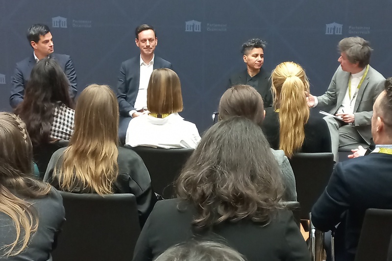 Diskussionsteilnehmer sitzen auf einem Podium vor einem Publikum im Parlament Österreichs.
