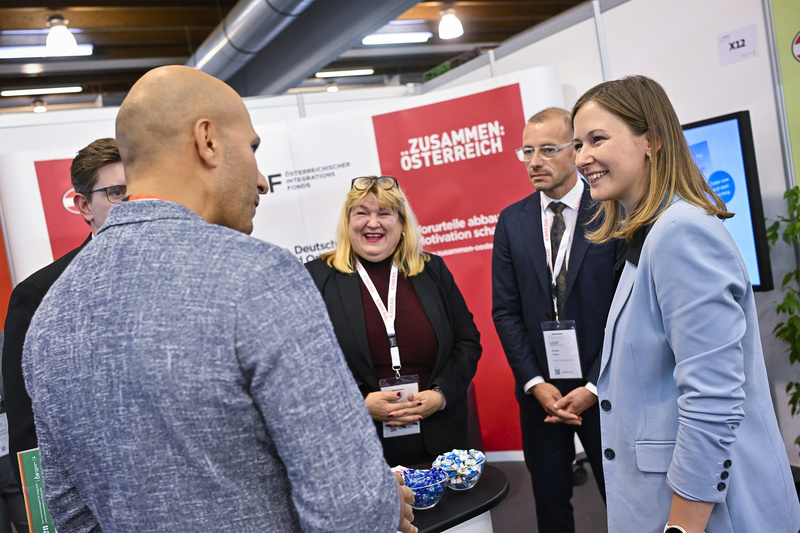 Fünf Personen stehen an einem Messestand, während sie miteinander sprechen und lächeln.