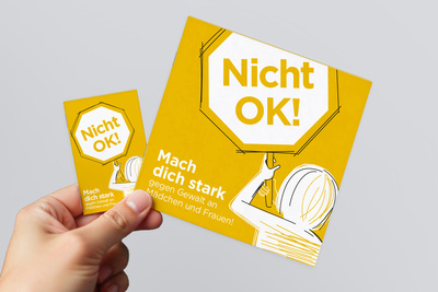 Eine Hand hält ein gelbes Plakat mit der Aufschrift "Nicht OK! Mach dich stark gegen Gewalt an Mädchen und Frauen!"