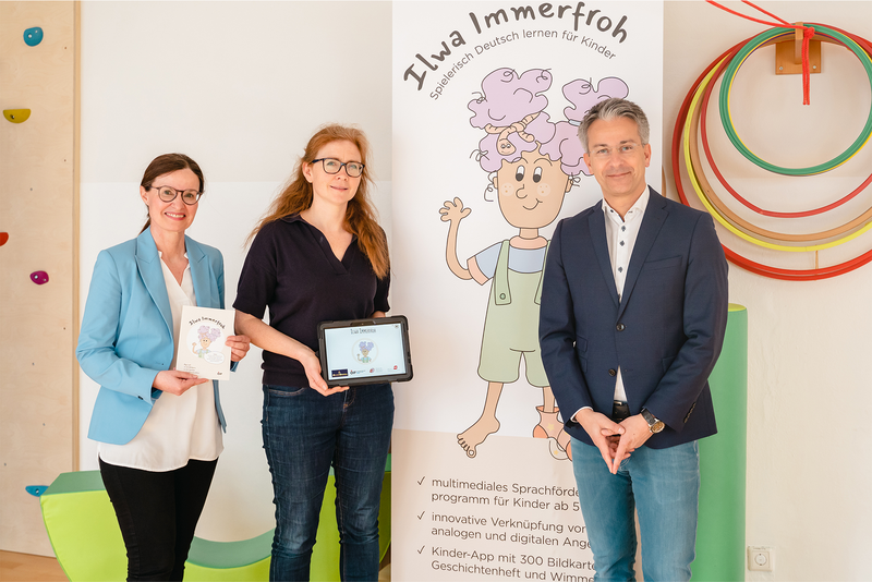 Drei Personen präsentieren das Projekt „Ilwa Immerfrohs“ zur Sprachförderung für Kinder.