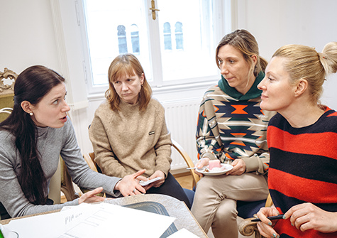 Vier Frauen in einem Gespräch, mit Notizen und einem Tisch als Mittelpunkt.