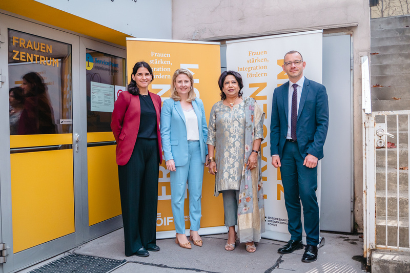 Vier Personen stehen vor einem Frauenzentrum, umgeben von Bannern zur Stärkung und Integration von Frauen.