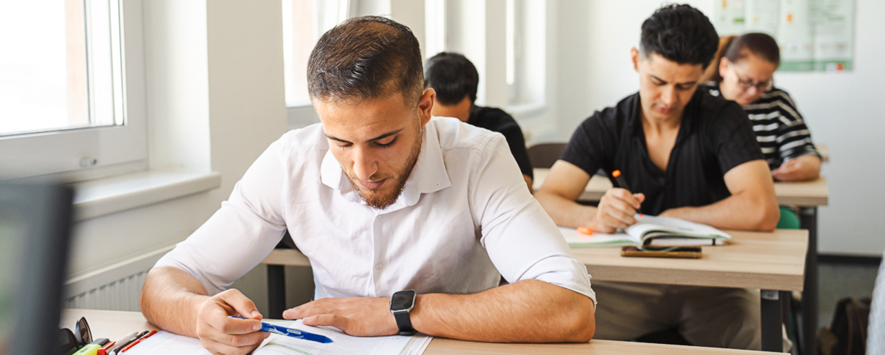 Teilnehmer/innen schreiben in einem Klassenraum