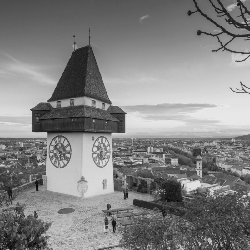 Uhrturm auf einem Hügel mit Stadtansicht im Hintergrund, in schwarz-weiß.