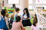 Eine Lehrerin sitzt im Kreis auf dem Boden und liest den Kindern ein Buch vor.