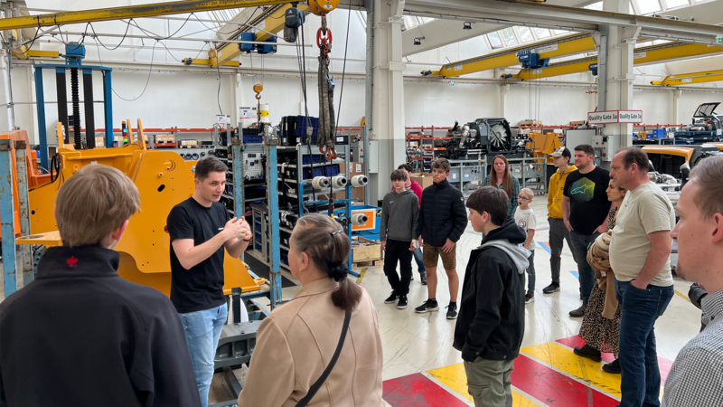 Eine Gruppe Menschen hört einem Vortrag über Maschinenbau in einer Werkstatt zu.