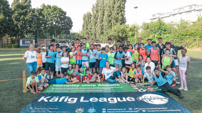 Eine Gruppe von Kindern und Jugendlichen posiert lächelnd auf einem Fußballfeld vor einem Banner.