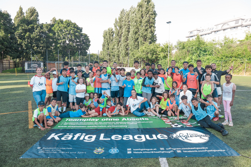 Eine Gruppe von Kindern und Jugendlichen posiert lächelnd auf einem Fußballfeld vor einem Banner.