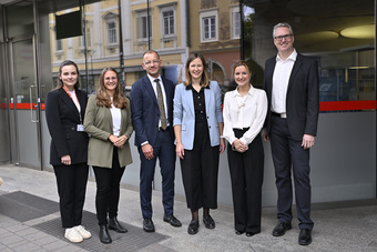 Sechs Personen stehen zusammen vor einem Gebäude und lächeln freundlich in die Kamera.