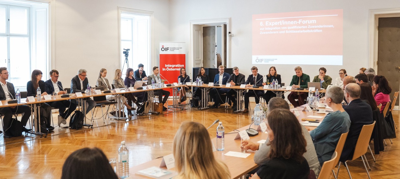 Es zeigt ein Expert*innen-Forum mit Teilnehmer*innen an einem großen Tisch in einem hellen Raum.