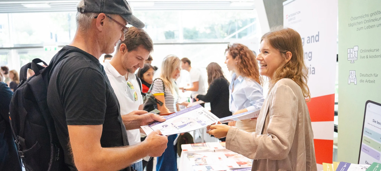 Menschen unterhalten sich an Ständen bei einer Veranstaltung, während sie Informationsmaterial austauschen.