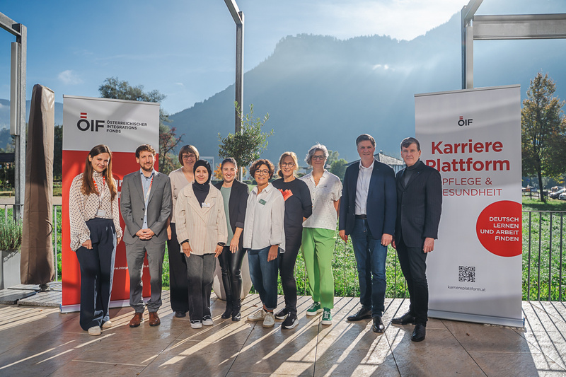 Gruppfoto von Personen vor Bannern der Karriereplattform Pflege und Gesundheit in malerischer Berglandschaft.