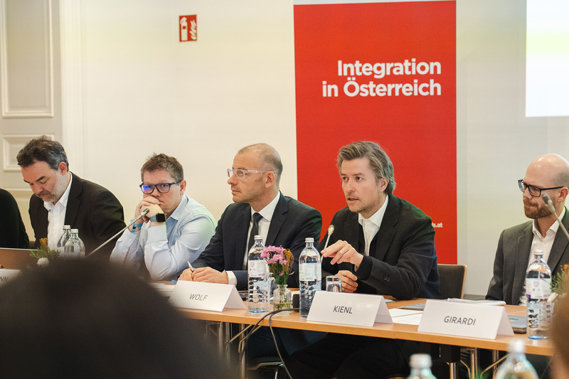 Die Teilnehmer diskutieren an einem Tisch, Hintergrund mit Banner „Integration in Österreich“.
