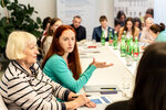 Zwei Frauen diskutieren an einem Tisch, umgeben von Teilnehmern und Getränken.
